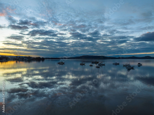 Aerial sunrise waterscape with boats, reflections and cloud filled sky