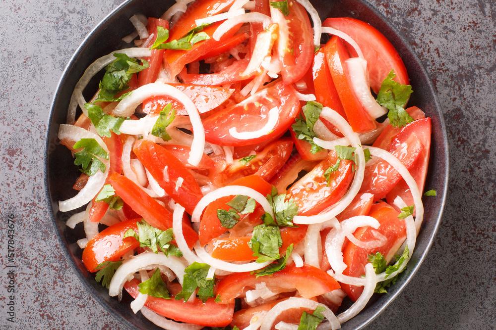 Vegetarian healthy tomato salad with onion and cilantro seasoned with olive oil close-up in a plate on the table. Horizontal top view from above Vegetarian healthy tomato salad with onion and cilantro seasoned with olive oil close-up in a plate on the table. Horizontal top view from above