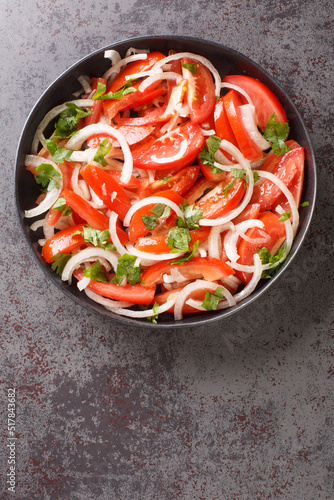 Summer tomato salad with onion and cilantro seasoned with olive oil close-up in a plate on the table. Vertical top view from above