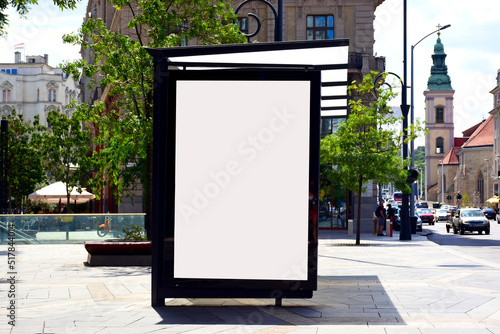 bus shelter at a busstop. blank billboard ad display. empty white lightbox sign. urban street setting. city transit station. glass and aluminum frame structure. outdoor advertising. green trees