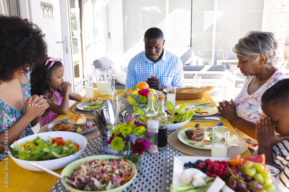 Multiracial multigeneration family with meal on table praying before having lunch at dining table