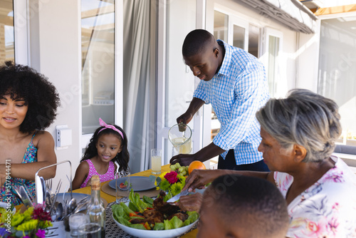 African american man serving drinks to multiracial family while having lunch at dining table at home