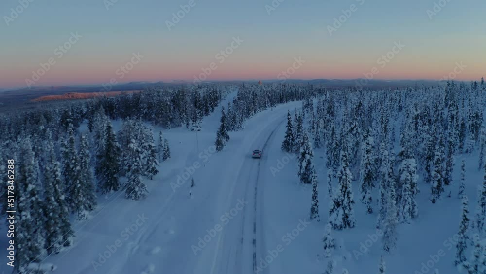 Aerial view following vehicle on journey through Lapland wilderness freezing Scandinavia woodland scenery at sunset Aerial view following vehicle on journey through Lapland wilderness freezing Scandinavia woodland scenery at sunset