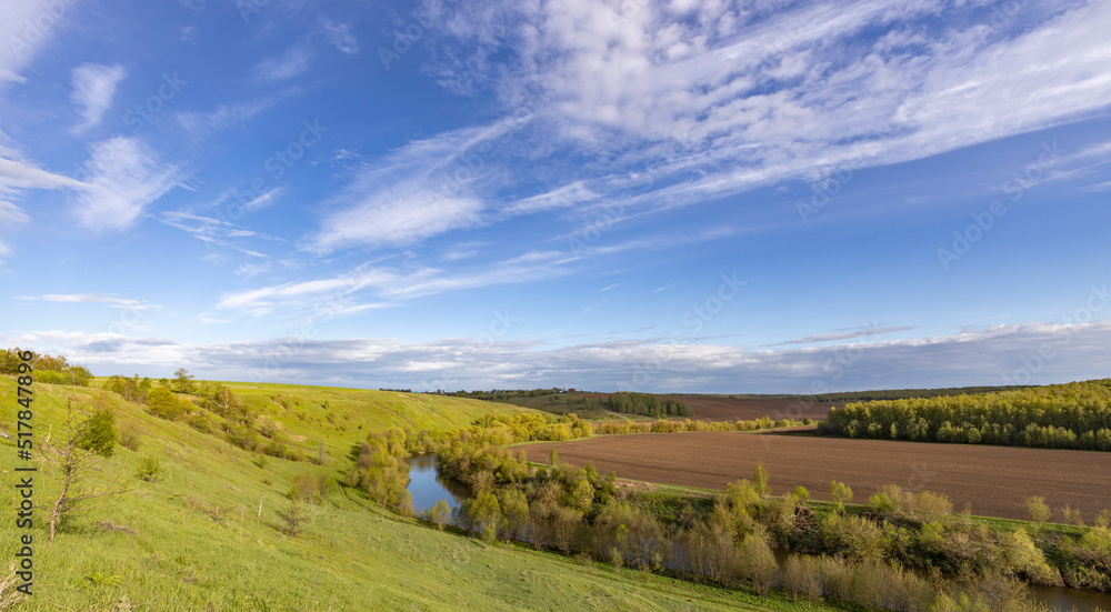 View of the countryside. bright greenery in the ravine. Saturated green grass against the blue sky. Plowed field on the horizon. Landscape with a small river in a ravine.