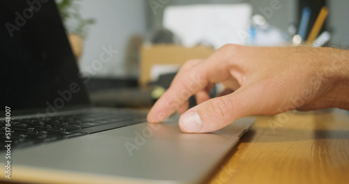 Male hand starts working touchpad of laptop. Click, zoom with your fingers, drive on the surface, spread your fingers. Side view, close-up, workplace.