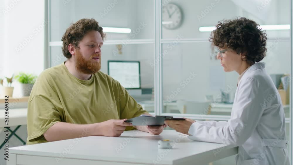 Young overweight man walking in medical office and having consultation with female doctor about weight loss Young overweight man walking in medical office and having consultation with female doctor about weight loss