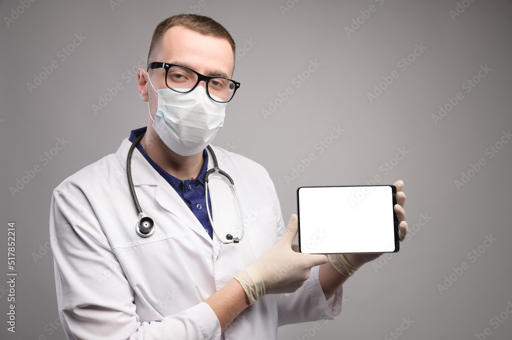 Confident doctor man shows a blank screen of a tablet computer, wearing a mask and glasses. Studio shot, copyspace Confident doctor man shows a blank screen of a tablet computer, wearing a mask and glasses. Studio shot, copyspace