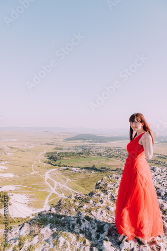 A girl in a red dress on the background of the mountains lifestyle. Illustrating articles about travel. A girl with a beautiful view. Vacation in Crimea. White rock. View of the villages. Lifestyle pr