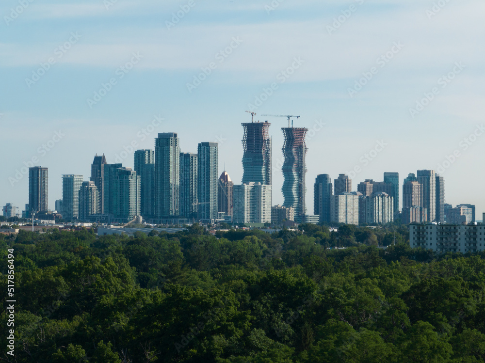 A modern cityscape skyline is seen on the horizon of a sunny day. New buildings and condos are under construction.