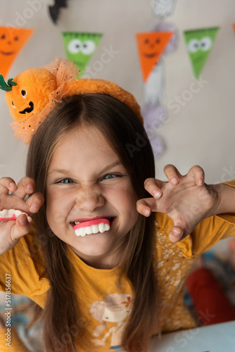 A little girl with vampire teeth is wearing an orange headband with a cute pumpkin. Halloween party. Boo photo