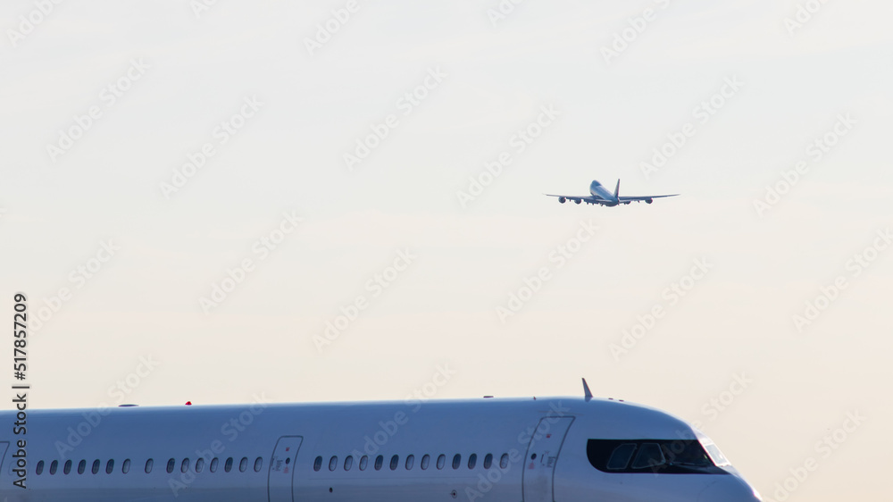 An airliner is seen taking off in the background, as another aircraft is seen passing by, close up on a clear morning. An airliner is seen taking off in the background, as another aircraft is seen passing by, close up on a clear morning.