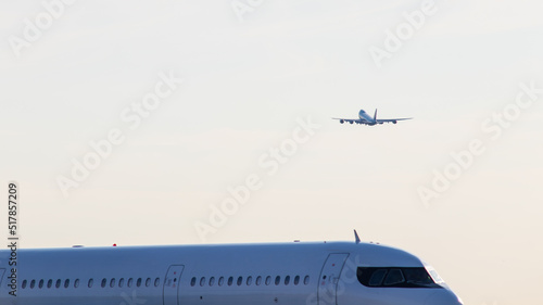 An airliner is seen taking off in the background, as another aircraft is seen passing by, close up on a clear morning.