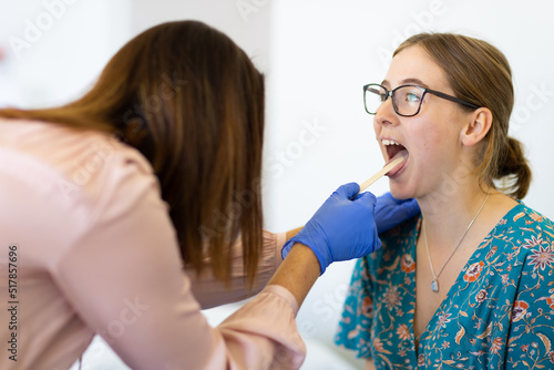 Young female with mouth open being checked by doctor