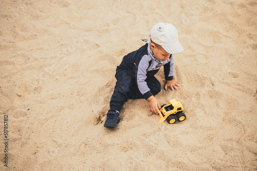 Child sitting in sandbox playing with toy. Little boy having fun on a playground. Summer outdoor activity for kid. Leisure time lifestyle childhood