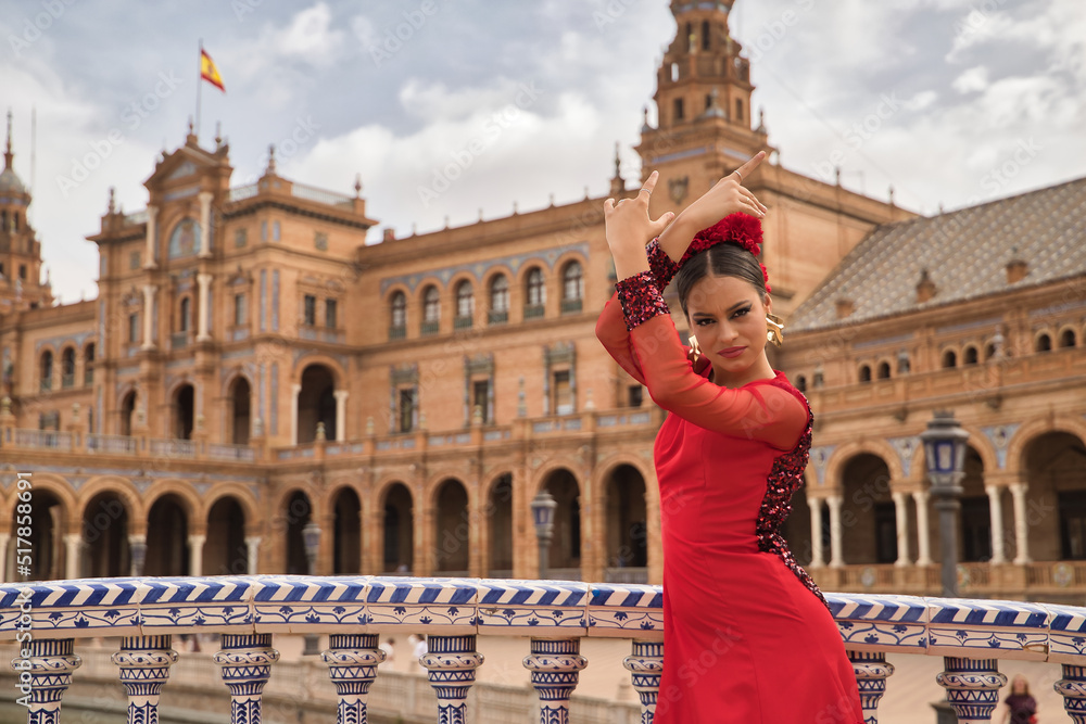 Fototapeta premium Young teenage woman in red dance suit with red carnations in her hair doing flamenco dance poses. Flamenco concept, dance, art, typical Spanish dance.