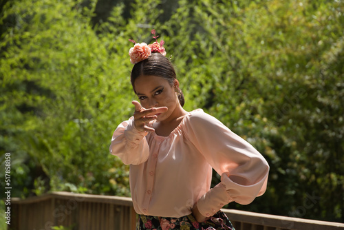 Portrait of young teenage woman in pink shirt, black skirt with flowers and pink carnations in her hair, dancing flamenco on wooden bridge. Flamenco concept, dance, art, typical Spanish dance.