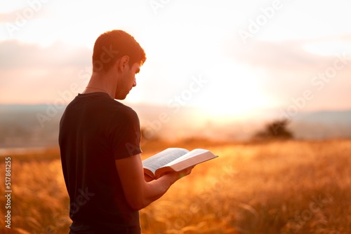Canvastavla Human praying on the holy bible in a field during beautiful sunset