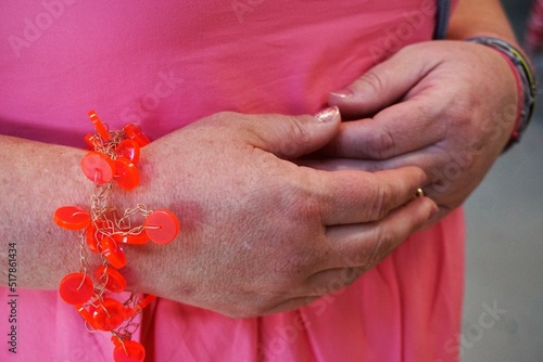 Frauenhände vor pinkem Sommerkleid und rot-orangenem Perlenarmband  photo