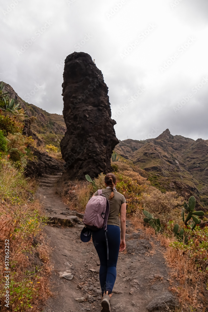 Woman walking next to massive rock formation wall in the Canyon Barranco de Afur, Anaga park, Tenerife, Canary Islands, Spain, Europe. Panoramic hiking trail from Afur to Taganana in Anaga massif