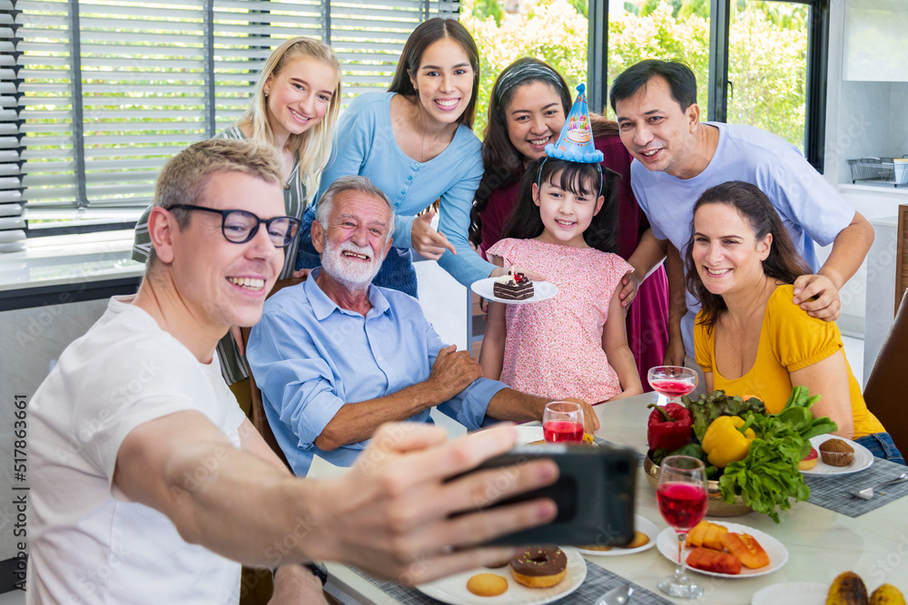 Father taking selfie photo using mobile phone for group photo in his daughter birthday party with whole big family and neighbor joining together in celebration meal