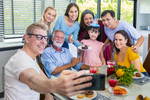Father taking selfie photo using mobile phone for group photo in his daughter birthday party with whole big family and neighbor joining together in celebration meal