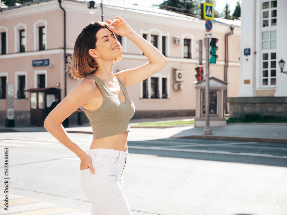 Young beautiful smiling hipster woman in trendy summer jeans and top clothes. Sexy carefree model posing on the street background at sunset. Positive brunette female. Cheerful and happy