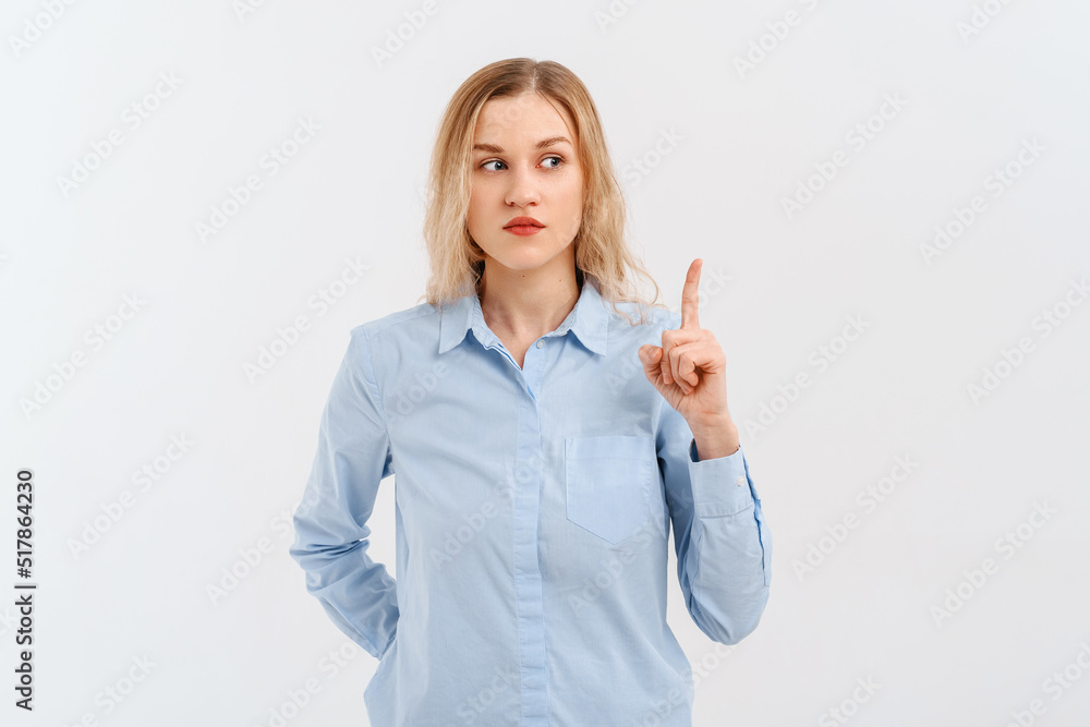 You better not. Serious blonde girl is frowning, pointing fingers up, stands in blue shirt. Indoor studio shot on white background You better not. Serious blonde girl is frowning, pointing fingers up, stands in blue shirt. Indoor studio shot on white background