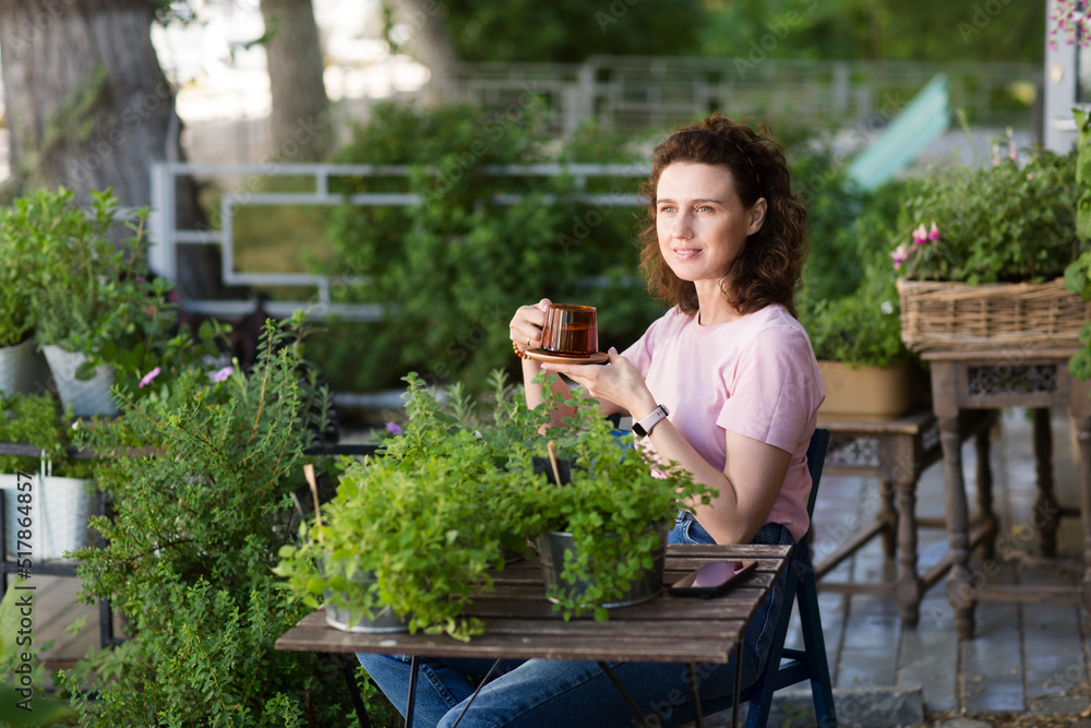 middle aged woman with a cup of tea relaxed in the garden with green fresh aromatic herbs near the house in summer. concept without stress. mental health. Slow life. Enjoying the little things. middle aged woman with a cup of tea relaxed in the garden with green fresh aromatic herbs near the house in summer. concept without stress. mental health. Slow life. Enjoying the little things.