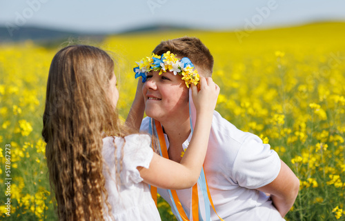 Sister puts on brother Ukrainian wreath with ribbons  against background of fields and sky
