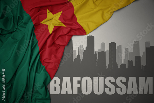 abstract silhouette of the city with text Bafoussam near waving colorful national flag of cameroon on a gray background.