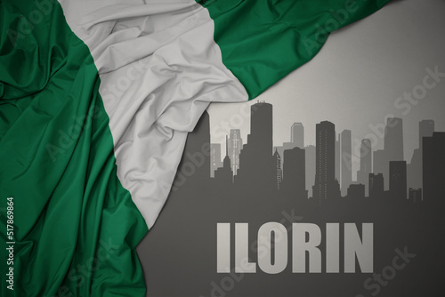 abstract silhouette of the city with text Ilorin near waving colorful national flag of nigeria on a gray background. photo