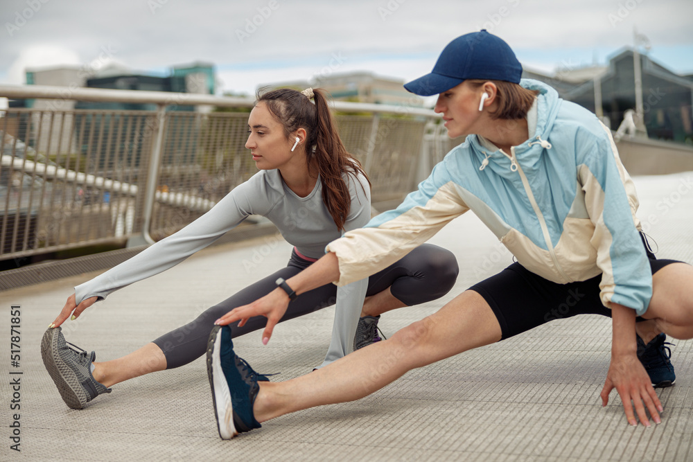 Beautiful sportive women doing stretching exercise on footbridge in the city 