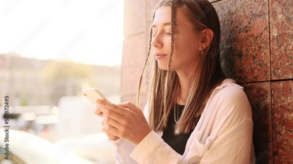Attractive caucasian woman hold smartphone, watching social media sitting in the street. Smiling young woman texting on her phone. Attractive caucasian woman hold smartphone, watching social media sitting in the street. Smiling young woman texting on her phone.