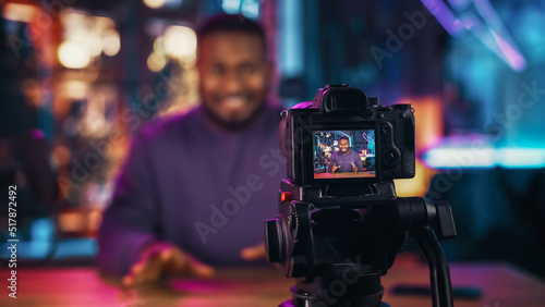 Handsome Young African American Man Talking Into Microphone While Recording Radio Show from His Loft Apartment. Happy Black Male Talking on Camera and Recording Podcast Live on Social Media.