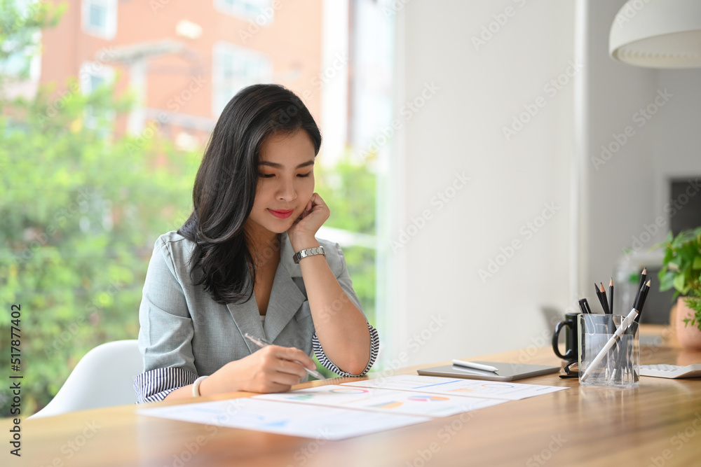 Concentrated asian female employee analyzing reports or solve business problem at workplace Concentrated asian female employee analyzing reports or solve business problem at workplace