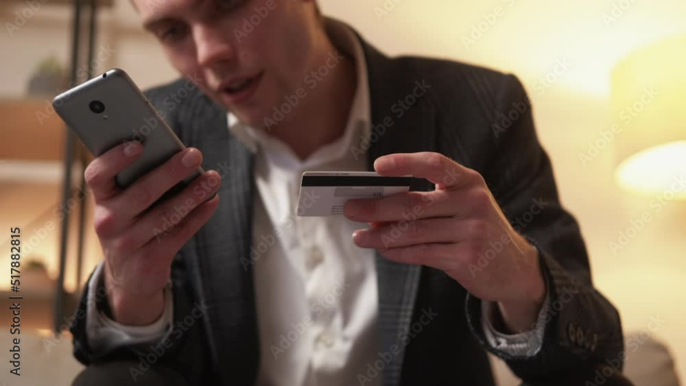 Mobile banking. Online transaction. Digital payment. Confident business man hands using credit card phone for Internet money transfer on defocused home interior. Mobile banking. Online transaction. Digital payment. Confident business man hands using credit card phone for Internet money transfer on defocused home interior.