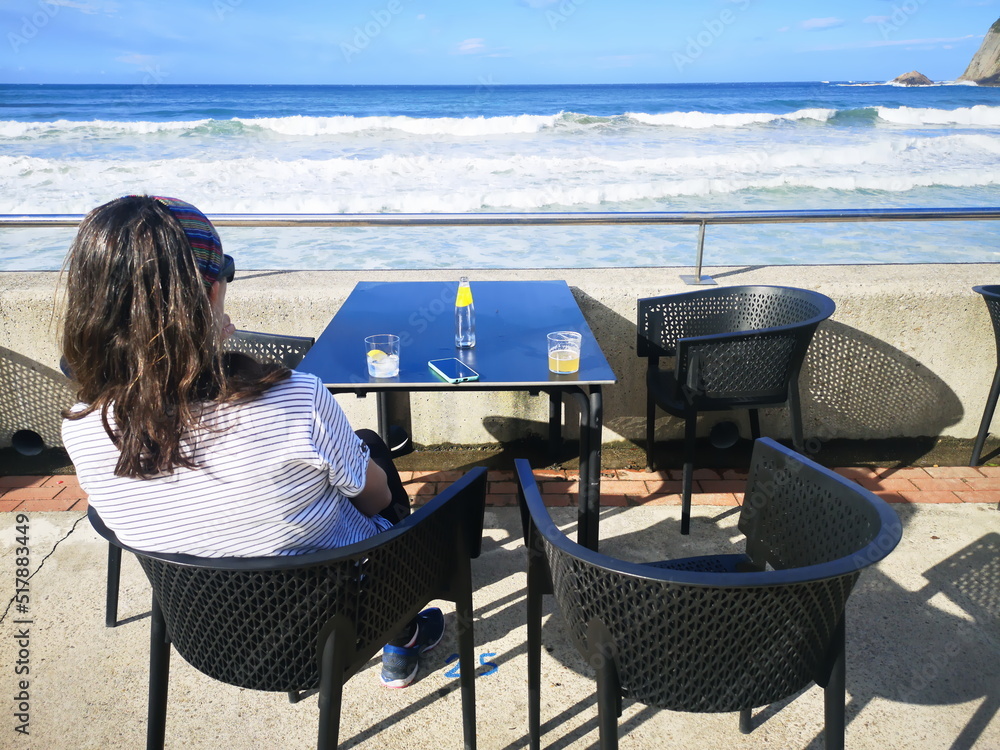 Obraz premium This is life, woman having a drink sitting on a terrace by the beach,
