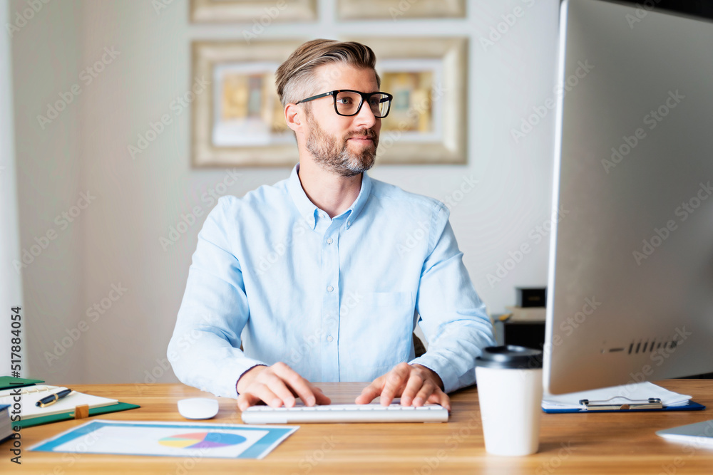 Handsome businessman using a computer while sitting at desk and working from home Handsome businessman using a computer while sitting at desk and working from home