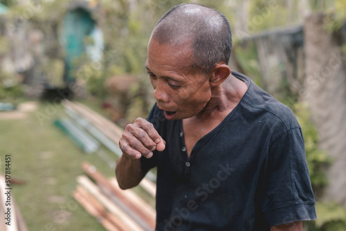 A thin balding man in his early 60s coughs while outside. Suffering from an itchy throat. photo