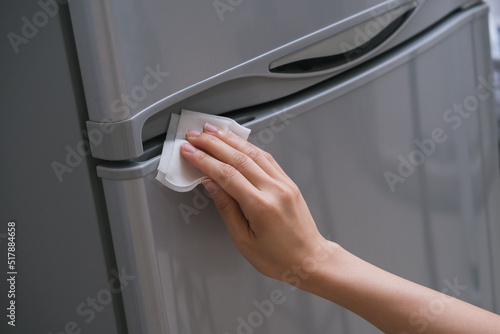 Ladies hand wiping the handle of the fridge door to prevent the spread of bacteria and virus. Personal hygiene concept.