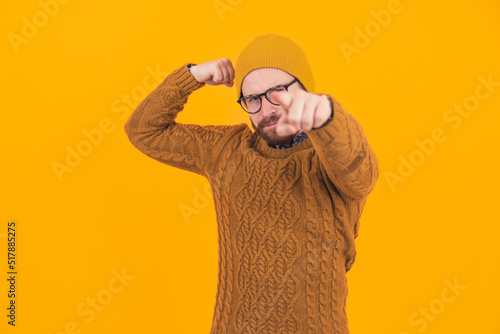 Stylish hipster flexing his muscles and pointing a finger to the camera over the orange background - physical and mental strenght concept. High quality photo photo