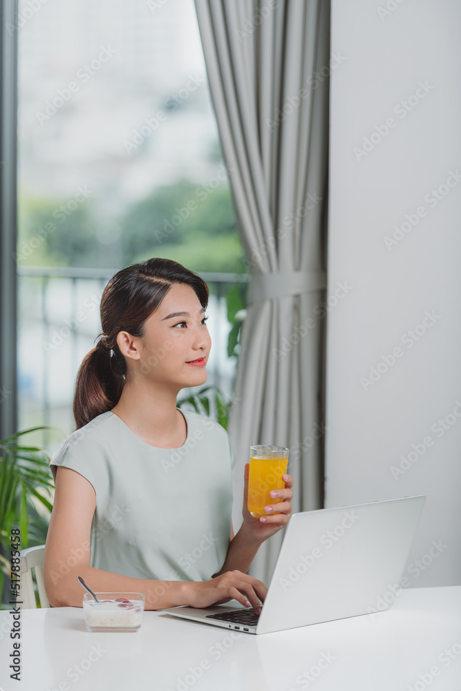 Beautiful woman relaxing with her laptop while holding a glass of orange juice Beautiful woman relaxing with her laptop while holding a glass of orange juice