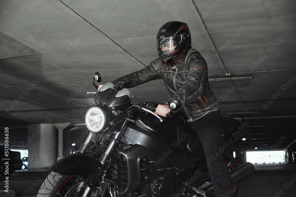 A man in a helmet sitting on a motorcycle in underground parking garage