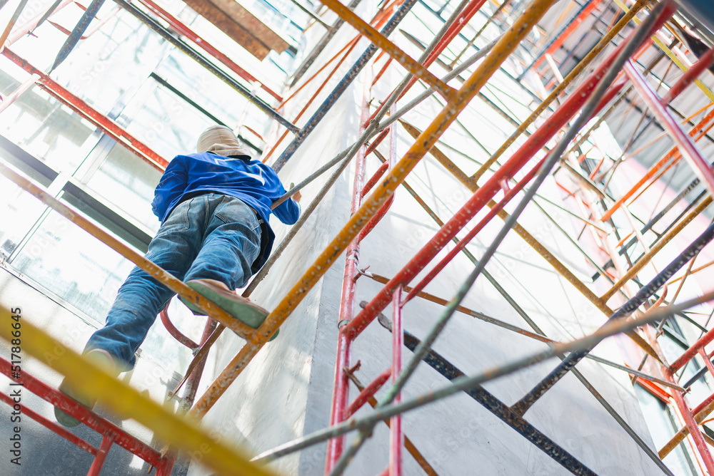 Construction worker climbs scaffolding in the job site without work safety equipment.