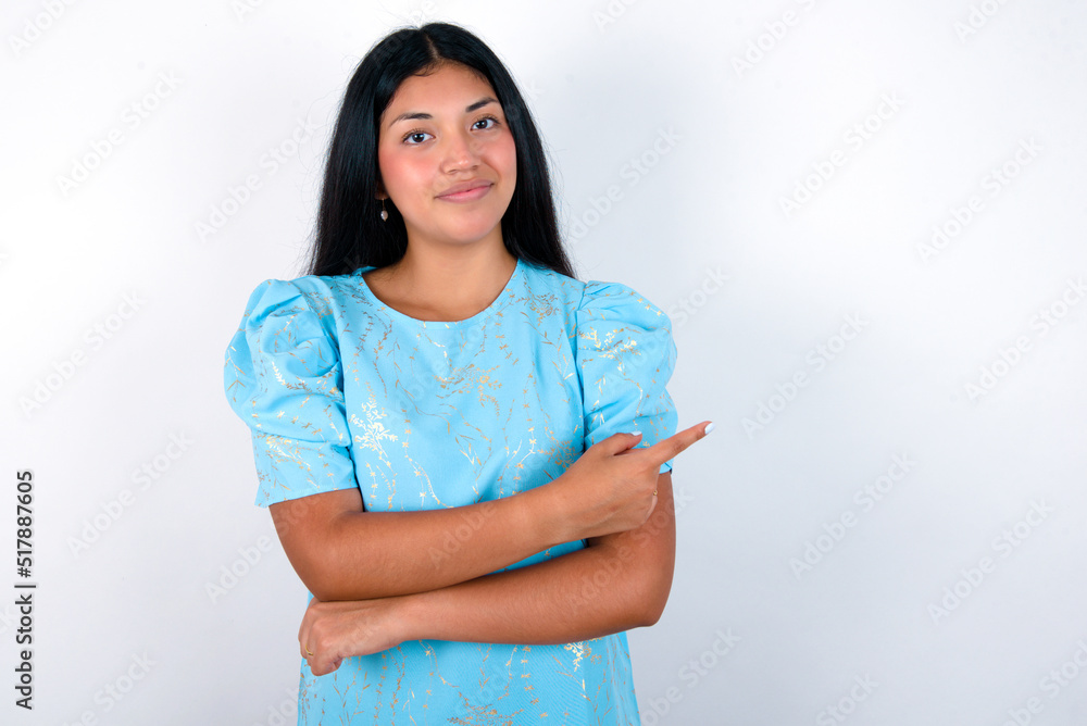 young brunette woman wearing blue T-shirt standing against white background smiling broadly at camera, pointing fingers away, showing something interesting and exciting. young brunette woman wearing blue T-shirt standing against white background smiling broadly at camera, pointing fingers away, showing something interesting and exciting.
