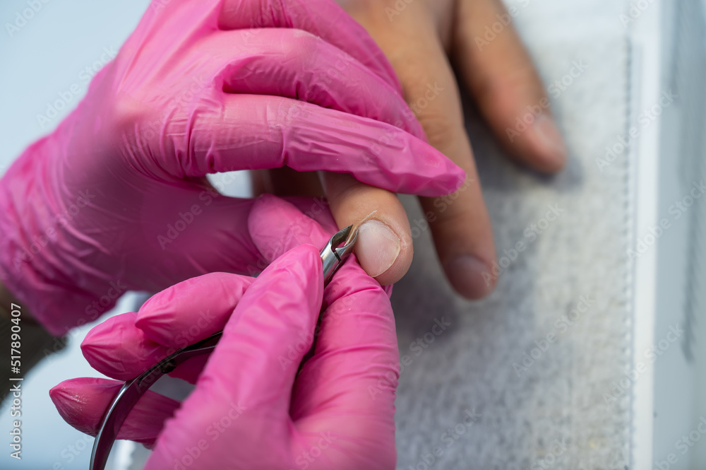 Manicurist cuts off cuticle to male client using nippers. 