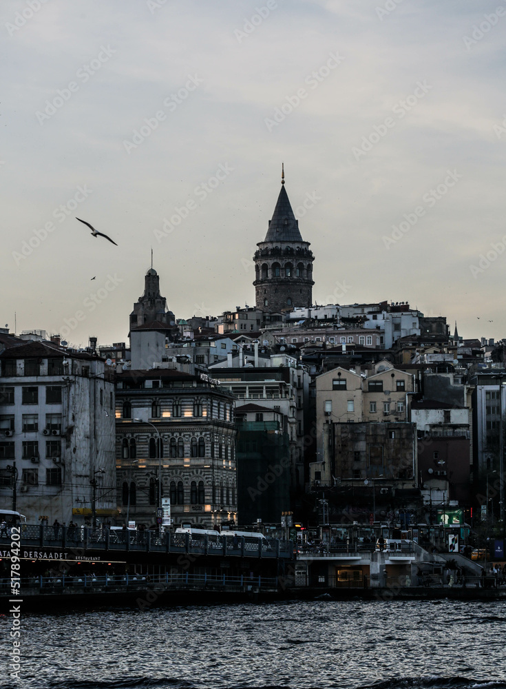 Fototapeta premium Istanbul, Turkey - April 2022: Medieval Galata Tower is famous landmark of Istanbul. Scenery of old historical place, panorama of Beyoglu district and ships on Golden Horn in the evening