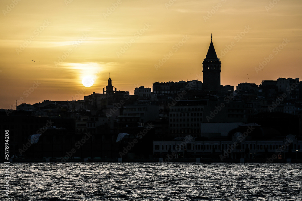 Istanbul, Turkey - April 2022: Dark silhoette of Medieval Galata Tower is  of Istanbul and Beyoglu district at sunset with yellow sky in the background