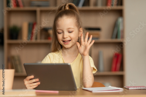Schoolgirl Waving Hello To Digital Tablet Making Video Call Indoors