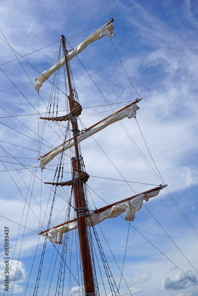 Tall ship mast with rolled sails, sky in background Tall ship mast with rolled sails, sky in background